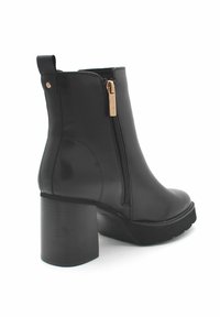 Botín negro de piel hasta el tobillo con tacón bloque, cremallera lateral con tirador dorado y tira de agarre en la parte posterior, sobre un fondo blanco.