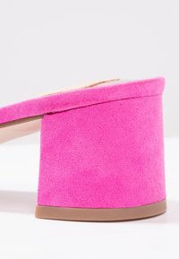 Chaussure à talon haut épais en suède rose vif avec semelle marron et bride supérieure beige sur fond neutre.