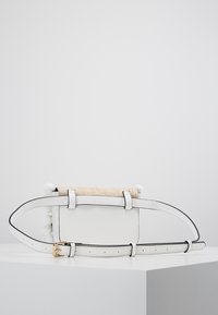 Borsa a mano bianca in pelle con parte superiore in paglia texturizzata. Caratterizzata da una tracolla sottile e una fibbia dorata, con pompon bianchi ai lati.