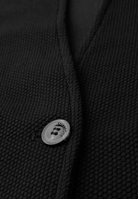 Zwarte textuur cardigan met een voorste knoopsluiting met een zilveren knoop met het label "StreetOne." Close-up van het materiaal en het design.