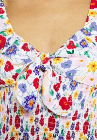 Abito floreale con un corpetto arricciato, cintura annodata e un motivo colorato con rosso, giallo, viola e verde su uno sfondo bianco.