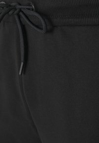 Černé tepláky s ribbaným pasem, stahovací šňůrkou a hladkým povrchem. Zaměření na pohodlí a volnočasové nošení.