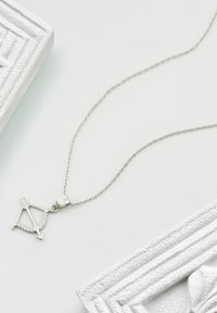 Silverhalsband med ett hänge i form av en pilbåge med små inbäddade stenar, fäst vid en delikat kedja.