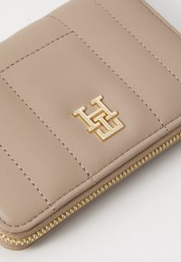 Beige skinn lommebok med quiltet design, gullhardwarens logo og en gullglidelåsdetalj langs kanten.