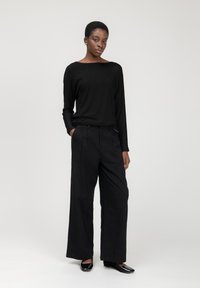 Maglietta nera a maniche lunghe, vestibilità rilassata; pantaloni neri a vita alta con ampie gambe e pieghe frontali; ballerine nere lucide. Design minimalista, tessuto liscio.