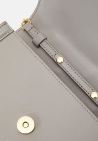 Grå lædertaske med guldfarvet hardware, der har en trykknaplukning og en syet stropfastgørelse. Glat tekstur med minimalistisk design.
