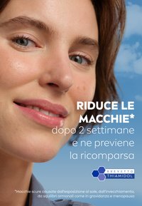 Primo piano del volto di una donna con pelle liscia e trucco leggero, capelli castani e un leggero sorriso. Lo sfondo presenta un cielo blu.