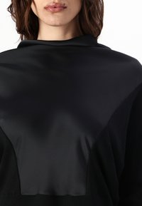 Czarny strój z satynowym, gładkim panelem na klatce piersiowej, kontrastującym z teksturowaną tkaniną po bokach i na dole. Prosty, nowoczesny design.