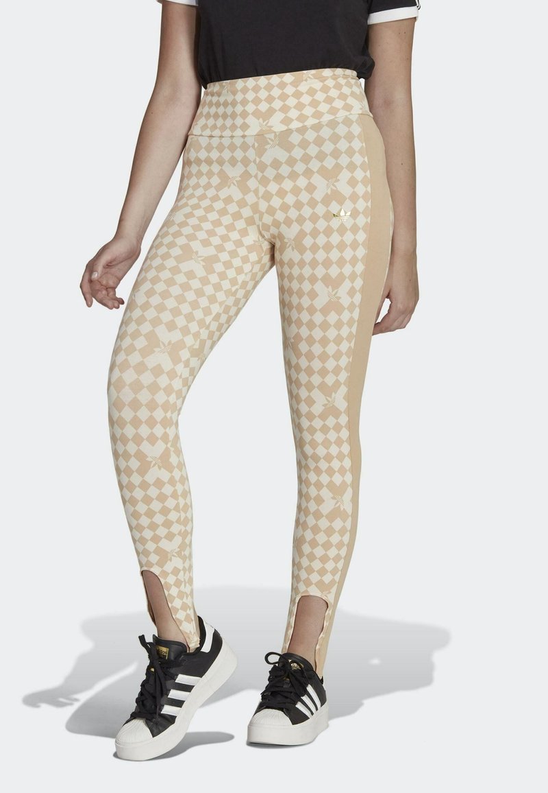 Legíny mají béžový kostkovaný vzor s květinovými detaily, bočními rozparky a vysokým pasem. Nosit s černobílými teniskami.