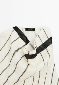 Tissu blanc avec des rayures noires, présentant un col en V et une surface texturée. L'étiquette indique "Massimo Dutti, fabriqué au Portugal."