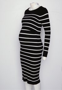 Mannequin enceinte portant une robe noire côtelée avec des rayures blanches horizontales irrégulières, des manches longues et un ourlet aux genoux.