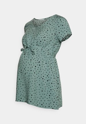 Abito da maternità in tessuto verde chiaro con pois neri, maniche corte, scollo a V e un dettaglio in vita annodato per una silhouette aderente.
