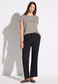 T-shirt gris clair à manches courtes avec un imprimé logo sur le devant, associé à un pantalon large noir à côtes et des chaussures plates en mesh noir.