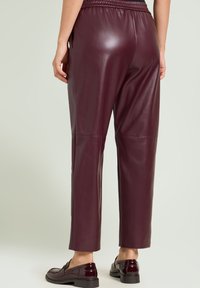 Bordeaux rood faux leren broek met een relaxte pasvorm, elastische tailleband en een gladde textuur. Voorzien van taps toelopende pijpen en subtiele naaddetails.