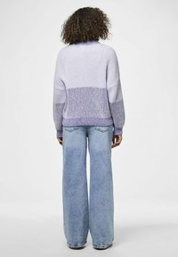 Pletena majica s gradientom od lavande do ljubičaste boje, s rebrastom teksturom i širokim rukavima, uparenim s laganim plavim trapericama širokog kroja.