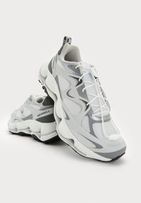 Pantofi sport gri și albi cu un upper din plasă texturată, accente de design circulare și talpă groasă. Prezintă șireturi ajustabile și brand.