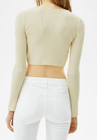Pull court beige côtelé à manches longues, avec un col rond. Porté au-dessus d'un jean blanc taille haute avec poches arrière.