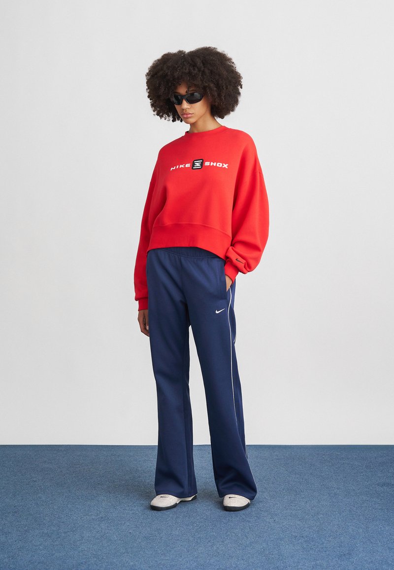 Felpa corta rossa con logo "NIKE SHOX", abbinata a pantaloni ampi blu navy con bande laterali bianche e logo Nike.