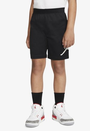 Barn iført sorte basketballshorts med hvid Jumpman-logo, sorte sokker og hvide sneakers med røde og elefantprint detaljer.