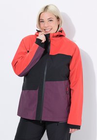 Giacca impermeabile rossa, nera e viola con cappuccio, chiusura con zip e due tasche laterali, caratterizzata da un design a blocchi di colore e polsini elasticizzati.