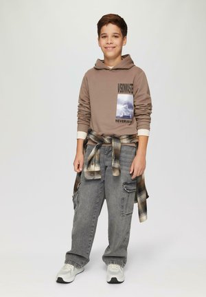 Bruine hoodie met grafische print, grijze cargobroek en een geruit shirt om de taille geknoopt. Witte sneakers met grijze accenten.