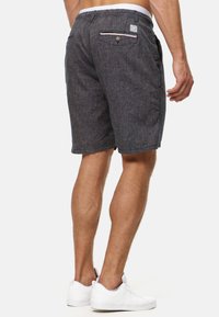 Grijze shorts van gestructureerde stof, met een achterzak en knoopsluiting en een gestreept accent, gecombineerd met witte sneakers.