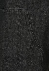 Musta farkkukangas, jossa on vino kudontakuvio, varustettuna yhdellä paikkataskulla ja hienovaraisilla ompeluyksityiskohdilla.