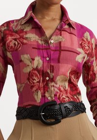 Floral-patterned shirt in shades of pink with a plaid background, featuring a button-up design and a black braided belt at the waist.