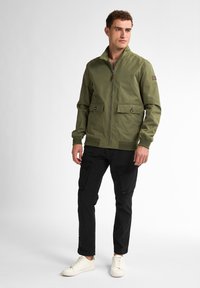 Jachetă bomber de culoare verde olive, cu închidere cu fermoar, două buzunare frontale, manșete tricotate și tiv ribborat, asortată cu pantaloni cargo negri și adidași albi.
