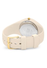 Orologio in silicone beige con fibbia in metallo dorato, cassa circolare e fondo trasparente. Marchio "ice watch" impresso sul cinturino. Design semplice.