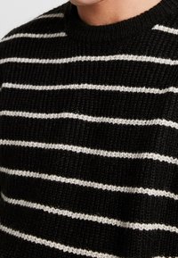 Czarnobiały sweter w paski wykonany z dzianiny, z poziomymi paskami, okrągłym dekoltem i teksturowanym wykończeniem.
