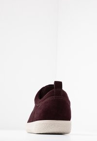 Burgundské semišové tenisky s texturovanou bílou gumovou podrážkou, se sloupkem na patě a prošívanými akcenty po straně.