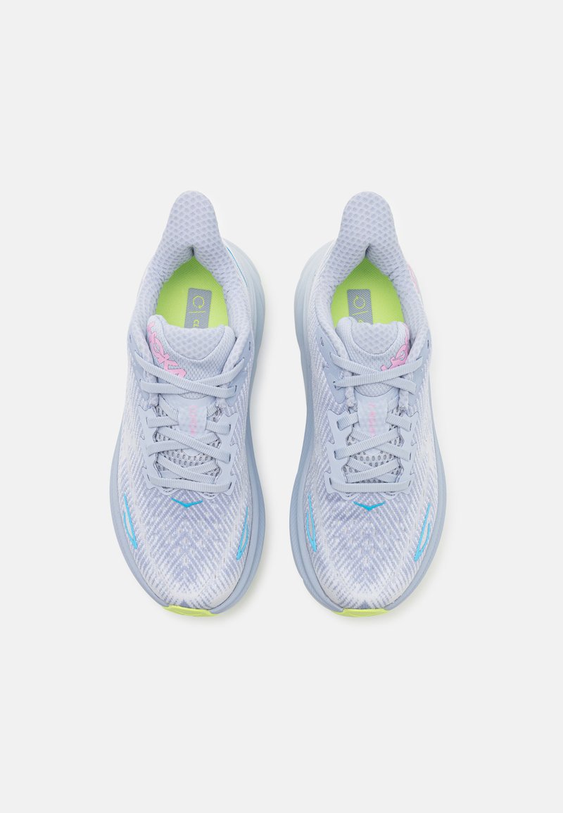 Hellesblaues Laufschuhpaar mit strukturiertem Mesh-Obermaterial, gepolstertem Kragen, weißer Sohle und grünen Akzenten auf der Einlegesohle und dem Logo. Schnürsenkel und Designelemente sind enthalten.