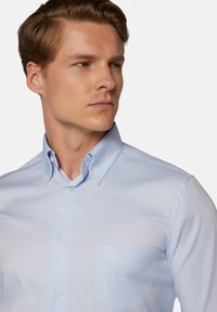 Svetlomodrá košeľa na gombíky s špicatým golierom, jednou náprsné vrecko, hladká textúra a jemný lesk na látke.