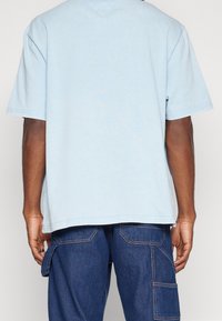 Camiseta de algodón azul claro de mangas cortas, con dobladillo recto y detalles de costura mínimos, combinada con pantalones cargo de mezclilla azules.