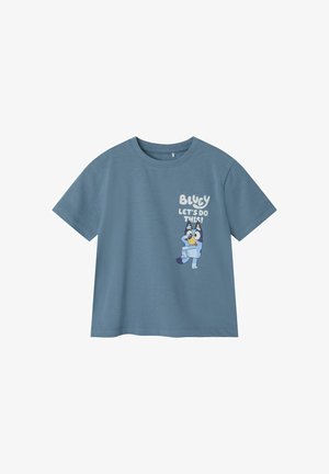 Lyseblå bomulds t-shirt med korte ærmer, med et tegneseriefigur og teksten: "BLUEY, LAD OS GØRE DET!" på forsiden.