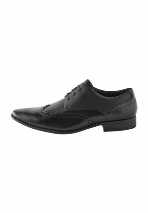 Zapato de vestir de cuero negro con punta afilada, paneles laterales de tela texturizada, detalles perforados y tacón plano. Diseño de cordones.