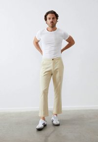 Beige bomullsbukser med rett snitt, med en enkelt knappåpning. Kombinert med en hvit tettsittende t-skjorte og hvite sneakers.