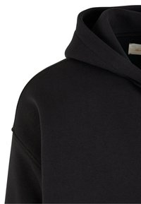 Sweat à capuche noir en tissu doux, couture d'épaule visible et détail de capuche pliée.