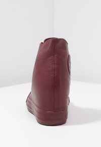 Stivaletto in pelle bordeaux con texture liscia, tacco arrotondato e branding discreto sul tallone. Cuciture visibili sul retro.