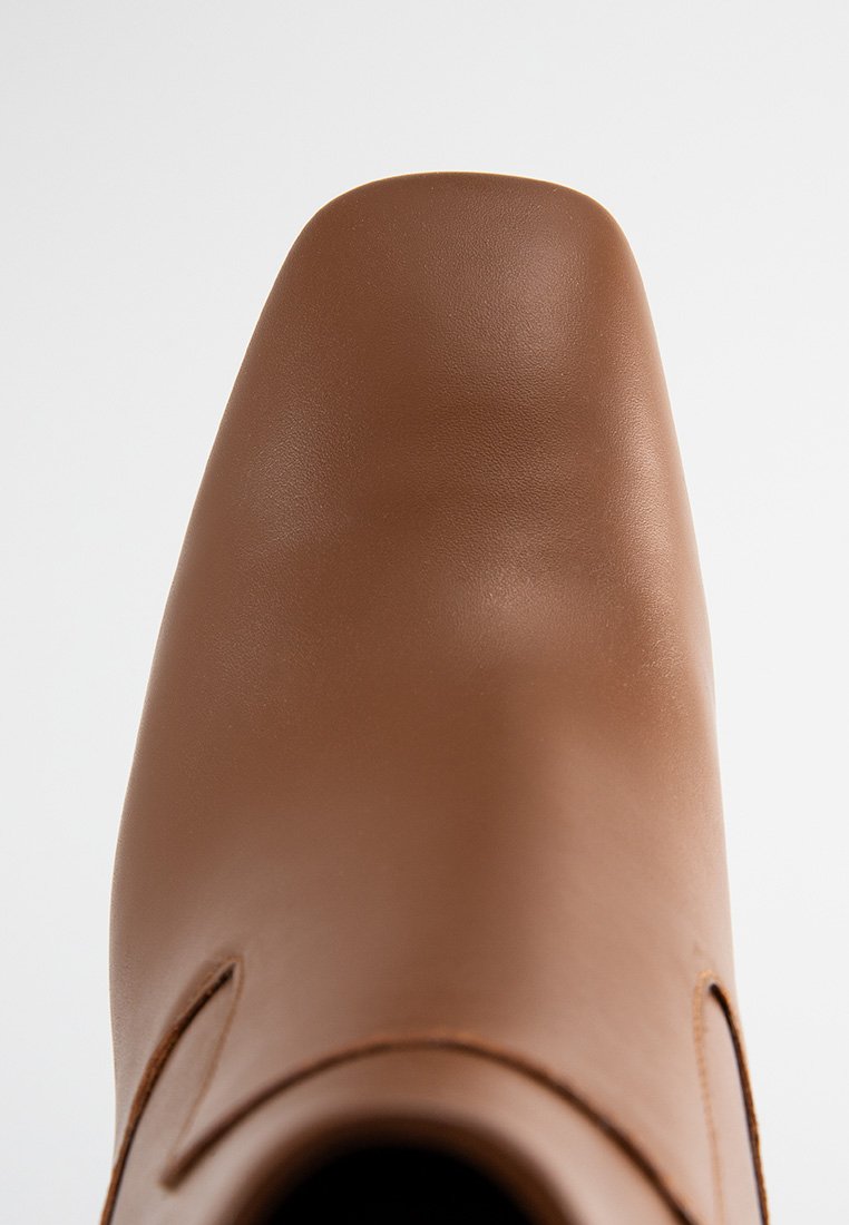 Chaussure en cuir marron avec une finition lisse et mate. Présente un bout carré et un minimum de détails de couture sur les côtés.