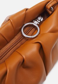 Braune Lederhandtasche mit gekräuseltem Design, ausgestattet mit einem silbernen Reißverschluss und Ringakzent, die eine weiche Textur und eine stilvolle Form zeigt.