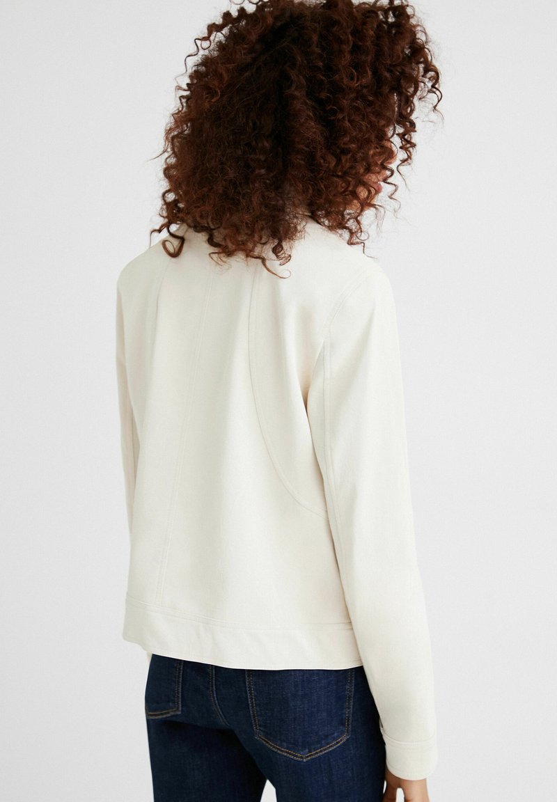 Lichtcrème jasje van zachte stof, met een ronde kraag, lange mouwen en een getailleerd ontwerp. Accenten met subtiele stikdetails.