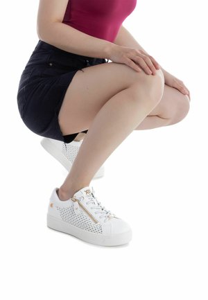 Zapatillas deportivas blancas con diseño perforado, con cierre de cremallera lateral y suela gruesa. Detalles en dorado, con cordones blancos y logo.