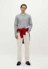 Pulover gri cu mânecă lungă și decolteu în V, pulover roșu legat în talie, pantaloni bej și pantofi negri. Design simplu, textură netedă și culori solide.