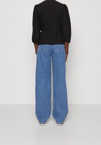 Sort bluse med pufærmer parret med højtsiddende, brede blå denimjeans med klassiske baglommer og en blød tekstur.