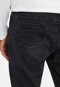Zwarte denim broek met meerdere achterzakken, een gestructureerde stof en een close-up van de tailleband en zakdetails.