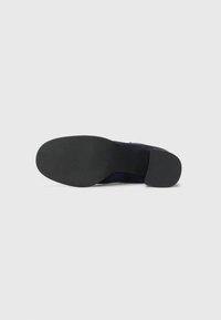 Black rubber outsole of a shoe, featuring a textured surface for grip. Upper material appears navy suede with a sleek, modern design.