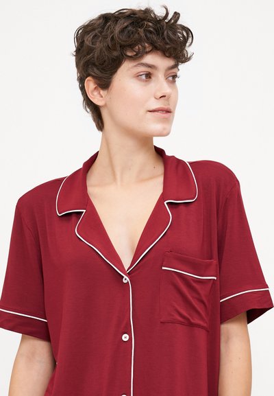 Burgundy short-sleeve pajama top with a notch collar, white piping, and a chest pocket. Soft fabric with a relaxed fit.