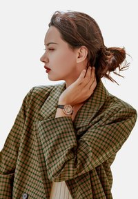 Blazer a cuadros marrones y verdes con un gran cuello, combinado con un reloj de pulsera negro que presenta una esfera redonda y adornos.